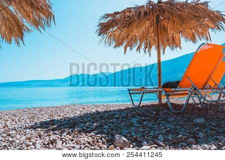 Prange Sunbed On Pebble Beach Under Straw Umbrella At Warm Sunset Light