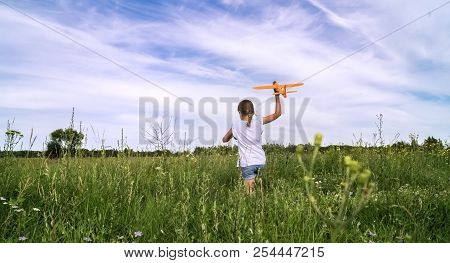 A Baby Girl Is Launching A Toy Airframe Glider In A Field Against A Blue Sky Background With Clouds.