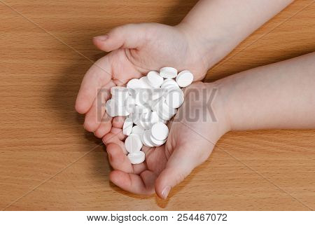 Pile Of White Pills In Hands Of Child Over Wooden Background. View From Above.