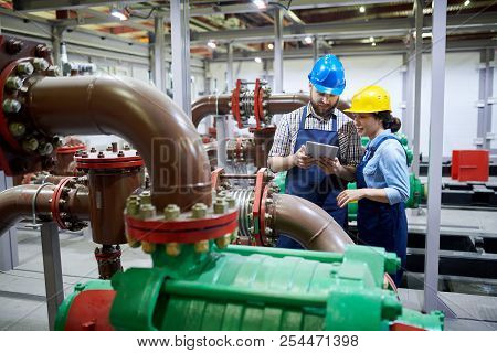 Portrait Of Two Factory Workers Using Digital Tablet While Working With Piping And Machines In Moder