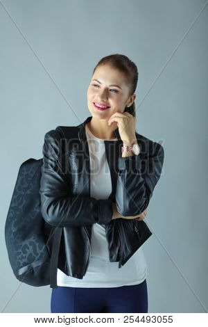 portrait of beautiful young brunette woman in stylish black jacket on gray.