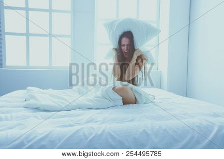 Young caucasian woman covering her head and ears with pillows.