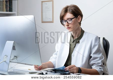 Female Practitioner Working At Modern Medical Doctor Office. Young Medical Doctor Taking Notes At Wo