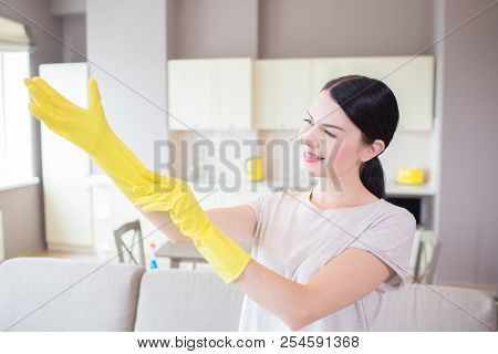 A Picture Of Woman Stands And Puts On Yellow Glove On Right Hand. She Looks At That And Smiles. Girl