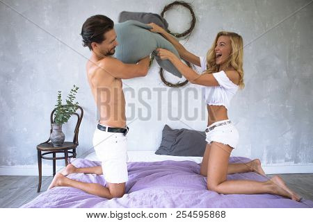 Young Beautiful Couple In White Fighting With Pillows On Modern Bed In Loft Design Bedroom ,having F