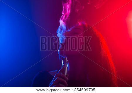 Young Woman In Neon Light And Smoke Of E-cigarettes Or Vape On Dark Background