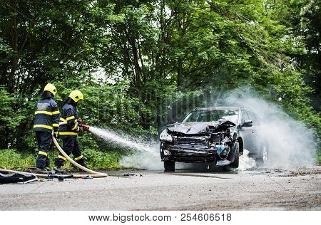 Two Firefighters Extinguishing A Burning Car After An Accident.