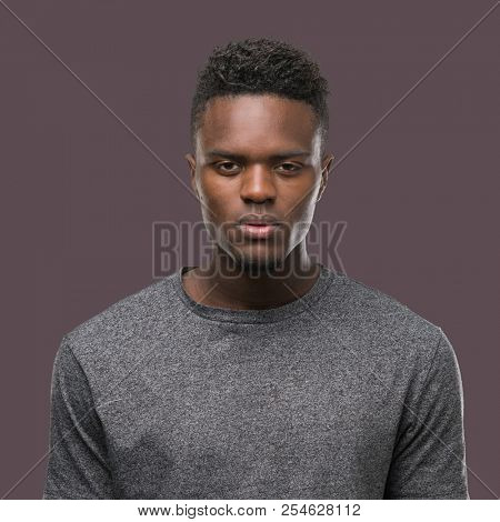 Young african american man wearing grey t-shirt with serious expression on face. Simple and natural looking at the camera.