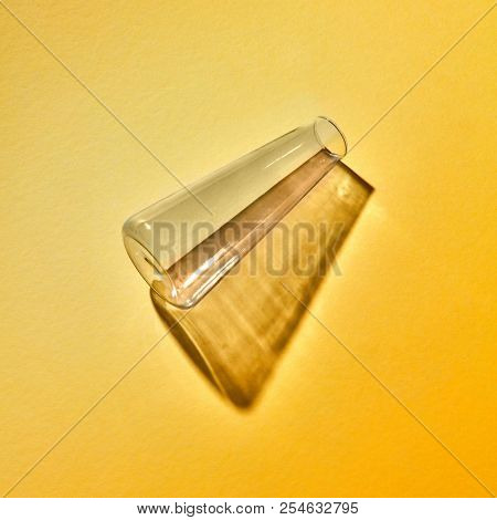 A glass flask empty with reflection and shadows lies on a yellow background, place for text. Laboratory tools for experiment. Laboratory concept.