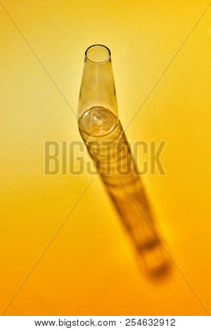 Empty glass transparent bottle with reflection on a yellow paper background, copy space. laboratory glasses at experiment in chemistry laboratory