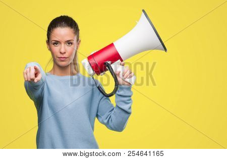Beautiful young woman holding megaphone pointing with finger to the camera and to you, hand sign, positive and confident gesture from the front