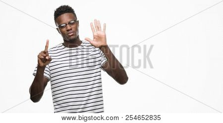 Young african american man wearing glasses and navy t-shirt showing and pointing up with fingers number six while smiling confident and happy.
