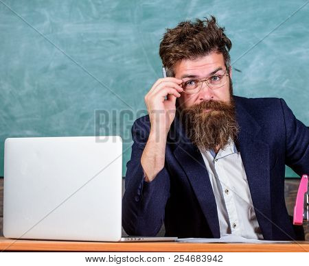 Examiner Full Of Doubts Sit At Table Chalkboard Background. Tricky Examinator Hesitates About Mark. 