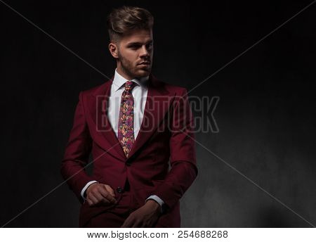 portrait of attractive man in grena suit resting on grey wallpaper background and looking to side