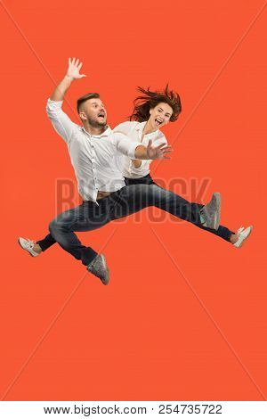 Freedom In Moving. The Happy Young Couple Jumping And Gesturing Against Red Studio Background. Runni