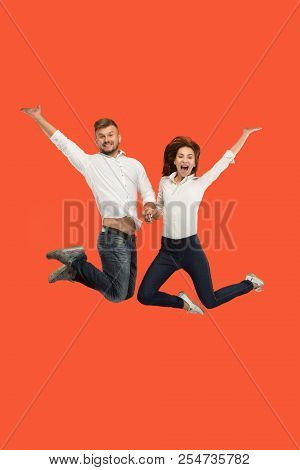 Freedom In Moving. The Happy Young Couple Jumping And Gesturing Against Red Studio Background. Runni