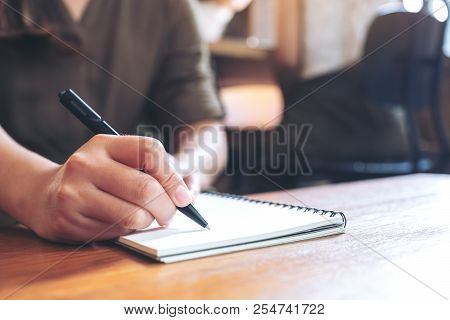 Closeup Image Of A Woman Writing Down On A White Blank Notebook On Wooden Table