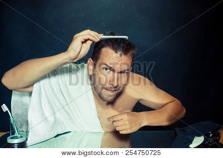 Man With Comb Concerned About Hair Loss. Close Up Photo Of Young Caucasian Man Looking On His Face. 