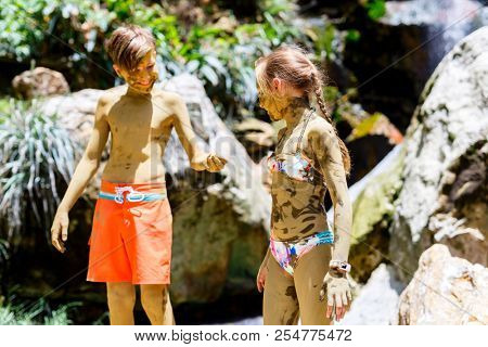 Kids brother and sister covered in mud in front of beautiful waterfall traditional tourist activity on St Lucia island in Caribbean