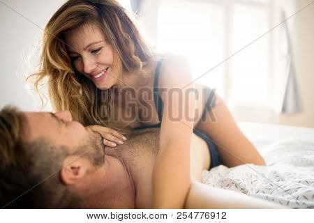 Back View Of Woman In Black Panties Holding Her Bra While Man Is Lying On Bed
