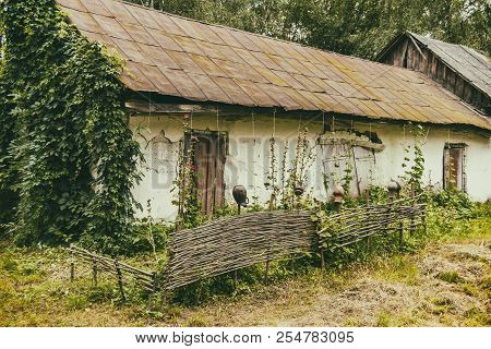 An Old House With A Fence In A Poor Village. Destroyed Building.