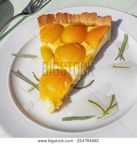Slice Of A French Baked Custard Tart With Apricots And Rosemary On A White Plate - Flan Parisien