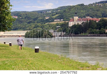 Man With Nordic Walking Poles Walking Along The Danube River In Front Of The Persenbeug Castle. Lowe