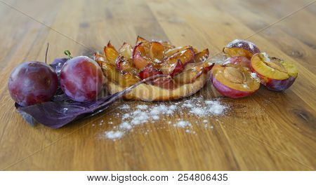 Fresh Plum Tartlet With Powdered Sugar And Plum On A Wooden Board.