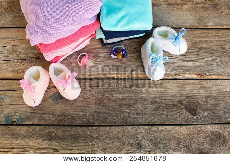 Baby Shoes, Clothing And Pacifiers Pink And Blue On The Old Wooden Background. Top View. Flat Lay.
