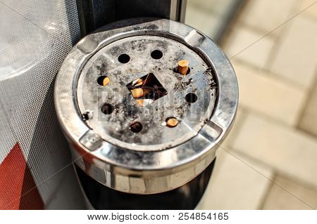 Sun Shining On Metal Ashtray Stand Outside Restaurant / Office, With Cigarette Butts And Ash. Smokin