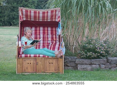 A Roofed Wicker Beach Chair And A Book, For The Attractive Woman The Time Stands Still