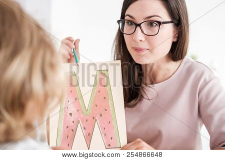 Close-up Of A Professional Child Development Therapist Showing A Prop Picture Of Letter 'm' To A Kid
