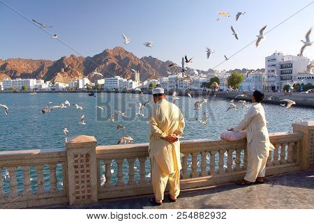 Muscat, Oman - January 28, 2012: Locals Feeding Seagulls At Muttrah Corniche With  Sur Al Lewatia Mo