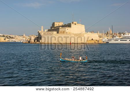 Fort St Angelo In Birgu Shot From Valletta. Tourists Swim In Traditional Maltese Boat In Grand Harbo