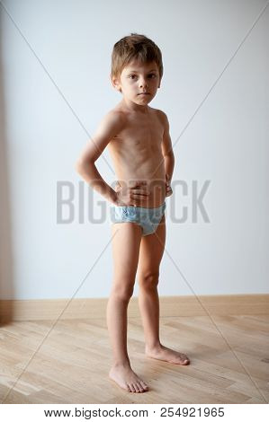 Strong Healthy Small Caucasian Preschooler Child In Shorts Showing Body Shape Indoors