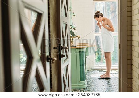 Side View Of Young Woman Standing On Digital Scales In Bathroom
