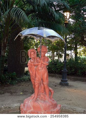 Sculpture Of Boy And Girl With Umbrella In The Garden Of Alameda Apodaca In Cadiz Capital, Andalusia