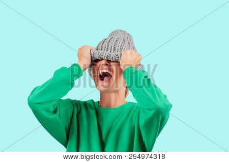 Furious. Emotional Angry Woman Is Pulling Wool Hat Over Her Eyes On Blue Background