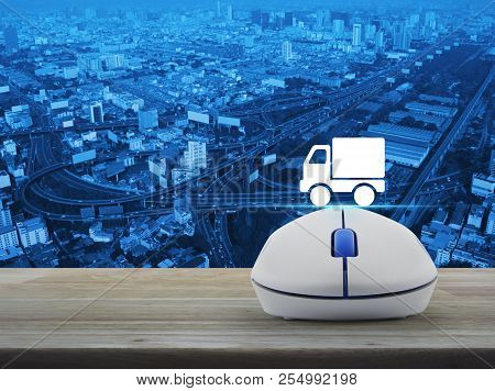 Truck Delivery Flat Icon With Wireless Computer Mouse On Wooden Table Over City Tower, Street, Expre