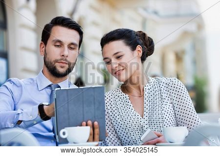 Businessman discussing plans over digital tablet to businesswoman while sitting and waiting for their food at restaurant