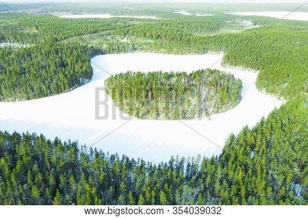 Aerial View Of Frozen Wild Forest Lake At Winter Time. Small Frozen Lake In Green Pine Tree Forest.