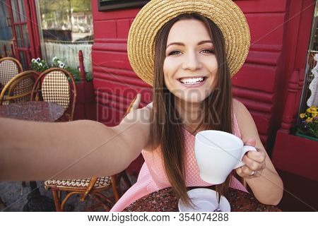 Selfie Time. Portrait Of Attractive Young And Smiling Woman In Pink Dress And Hat Holding Camera And