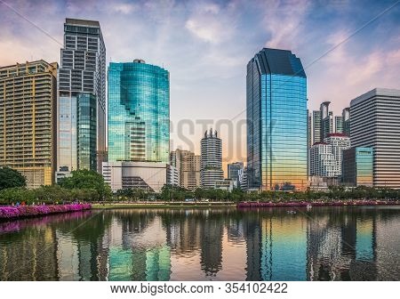 Skyscrapers Reflected In A Lake At Twilight. Benjakiti Park In Bangkok, Thailand