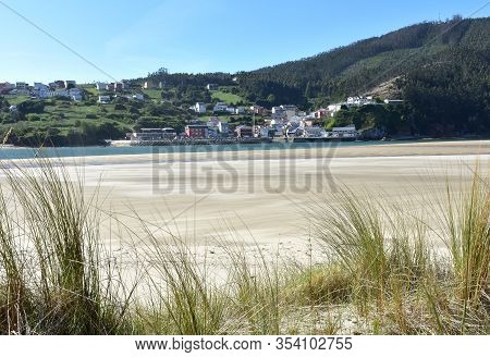 Small Fishing Village From Beach With Grass On Sand Dunes. O Barqueiro Or El Barquero, Galicia, Spai