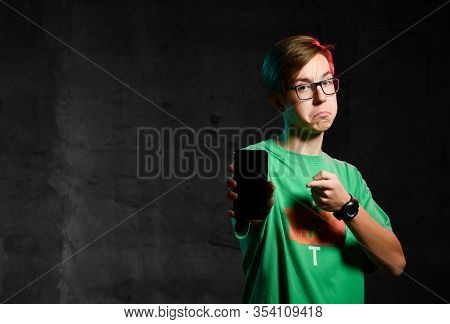 Young Teen Boy In Green T-shirt And Glasses Standing, Showing His Phone Screen And Feeling Disappoin