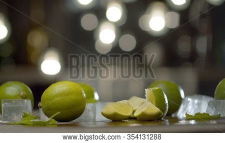 Close Up Sliced Limes On The Table Over Background Of Blurry Light Bulbs. Cooking Of Refreshing Drin