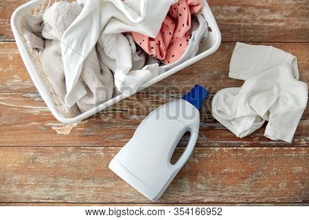 laundry, wash and housekeeping concept - baby clothes in basket with detergent or conditioner bottles on wooden table at home