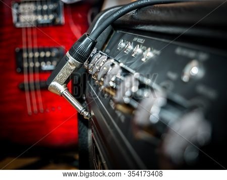 Guitar Cable With Jack And An Amplifier With A Red Guitar In The Background.