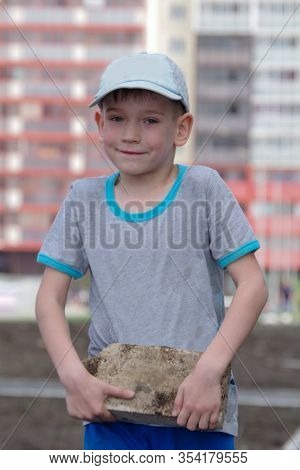 Caucasian Boy In A Gray T-shirt And Cap Helps Parents Carry Stones. Game Of Children. Helping Parent