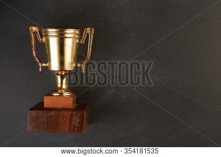 Golden trophy over blackboard background. top view. flat lay.Trophy is a specific achievement, serves as recognition / evidence of merit, awarded for sporting events